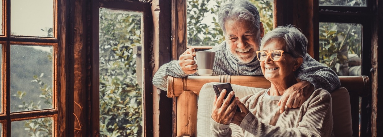 Een paar twee oude en volwassen mensen die thuis samen de telefoon gebruiken op de bank.